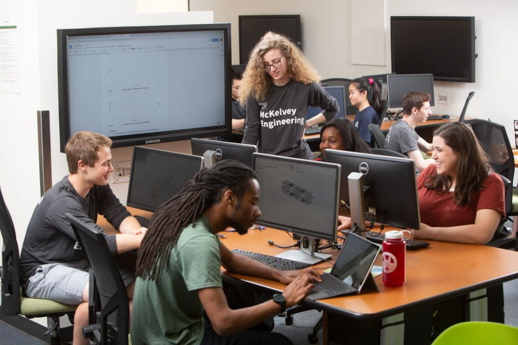 Students gather around computers working in a computer lab setting